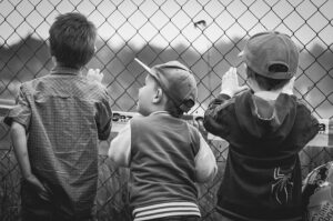 Three young boys watching a ball game through the chain link fence